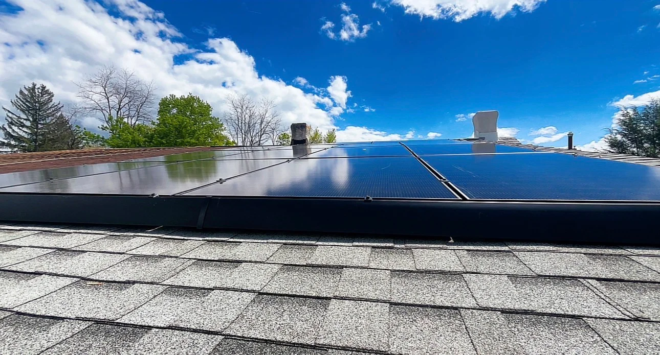Multiple blue solar panels installed on residential roof with clear sky and trees visible
