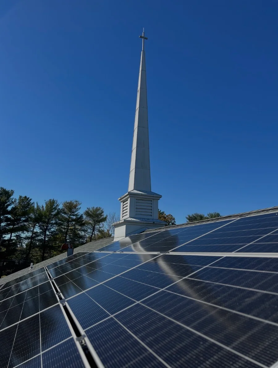 Solar panels installed on church roof with white steeple and cross visible against blue sky