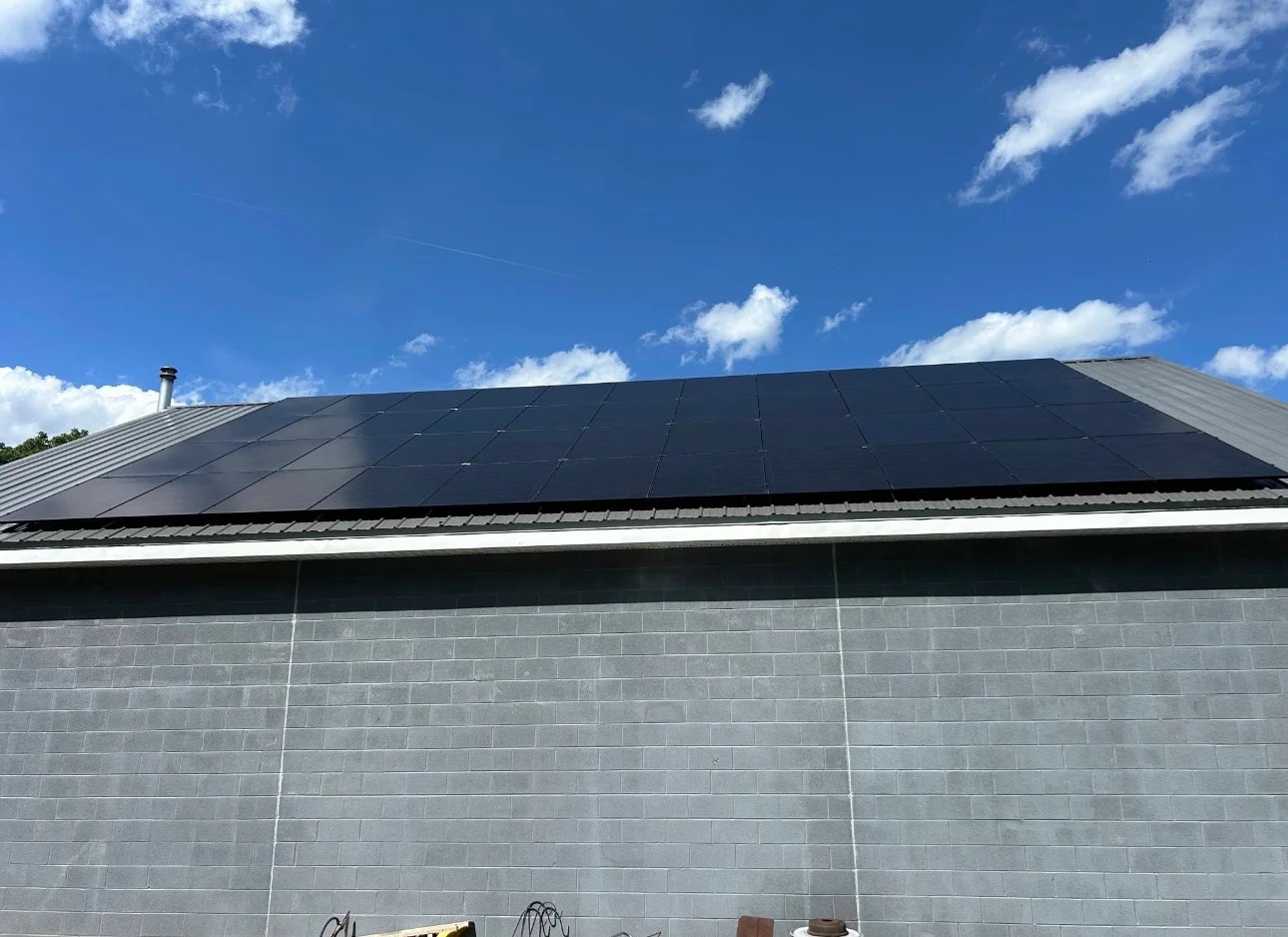 Black solar panels installed on residential roof with metal trim and clear blue sky