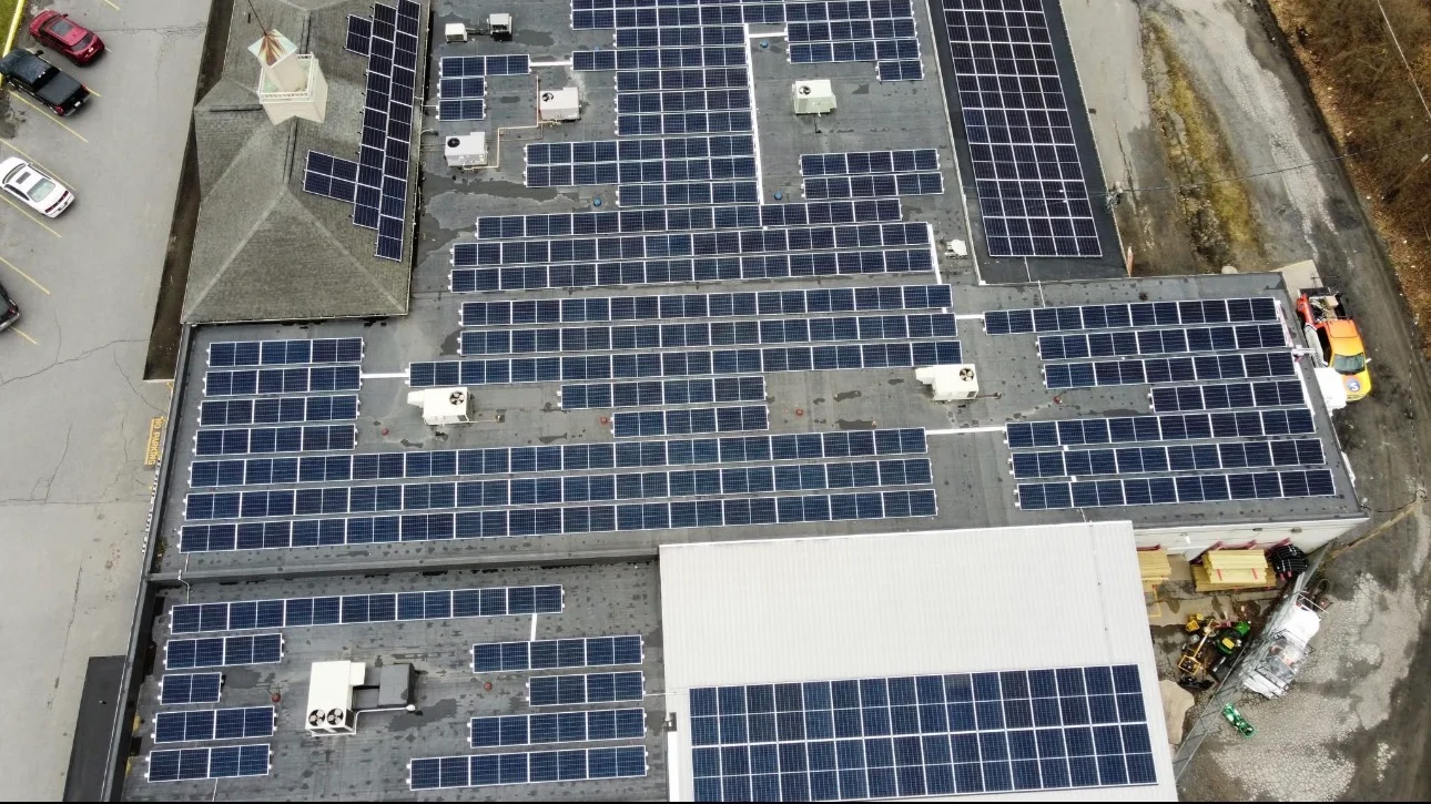 Aerial view of commercial rooftop with hundreds of solar panels and white inverter boxes