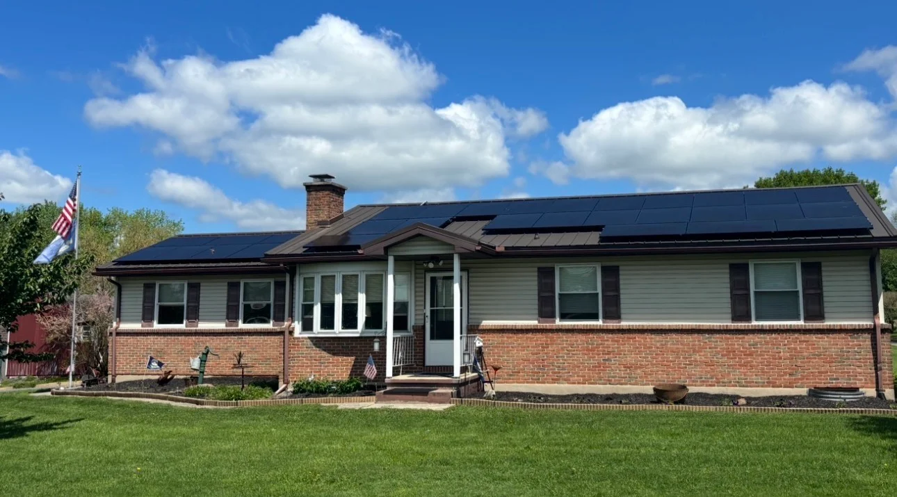 Solar panels installed on brick ranch home with green lawn and blue sky
